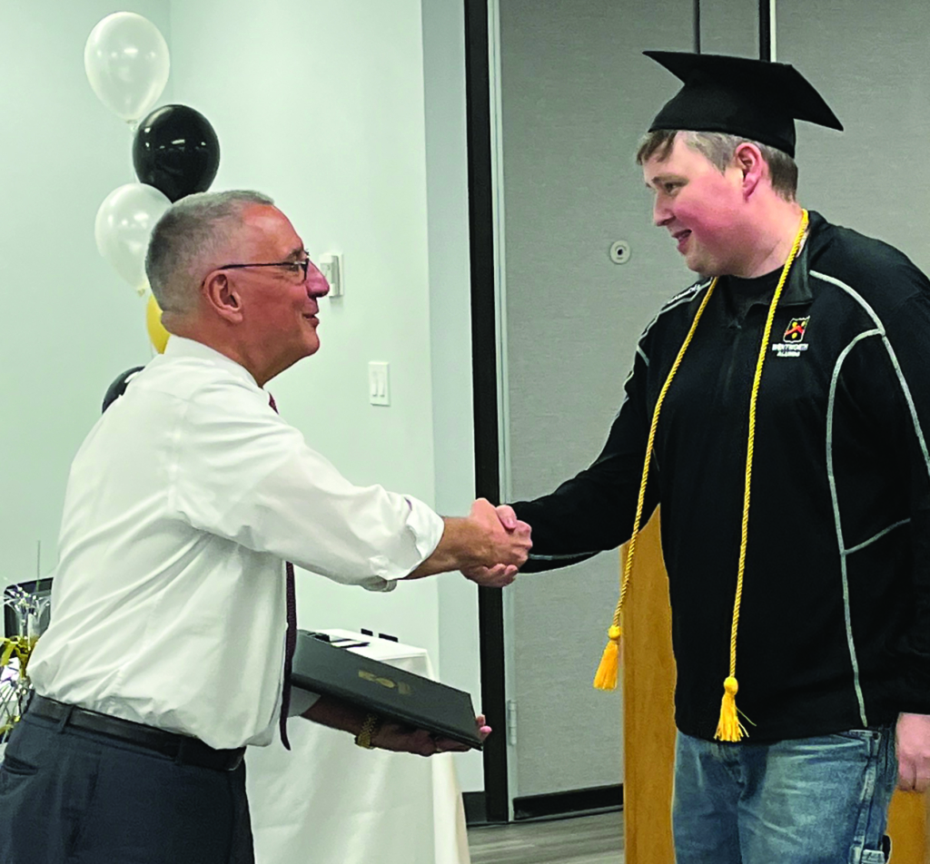 A man in a graduation cap shakes hands with an older man in a white shirt.