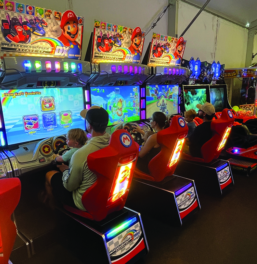 People playing colorful arcade racing games indoors.