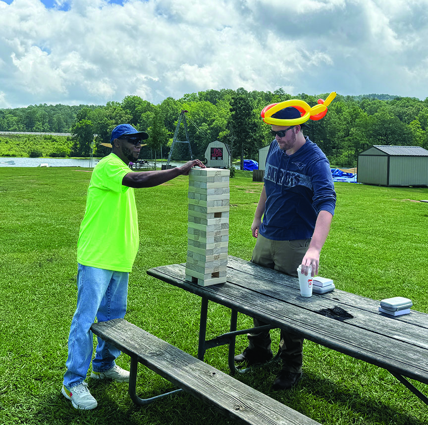Two men playing a giant outdoor Jenga game on a picnic table.