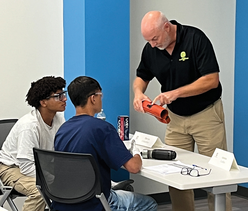 Instructor demonstrating a device to two students in a classroom.
